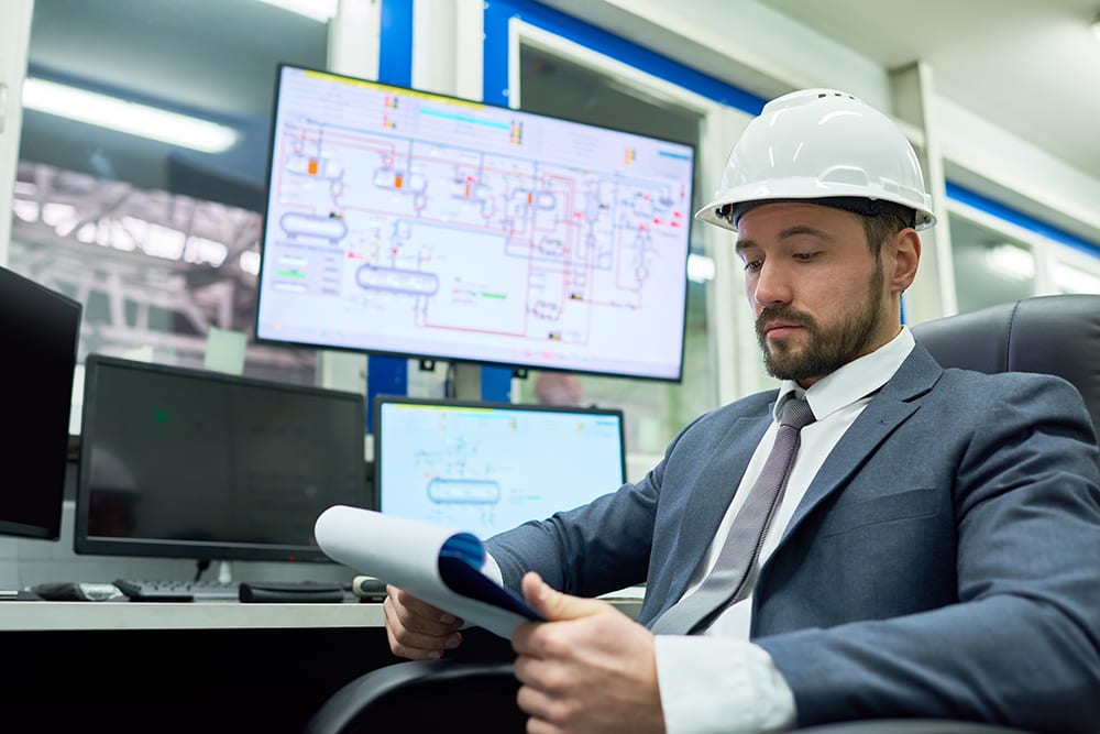 man wearing white hard hat reviewing reports on clipboard