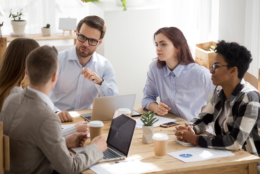 small group of employees siting around table discussing work